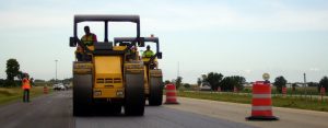 Two Sakai three wheel static asphalt rollers in an echelon pattern on a highway paving job site.