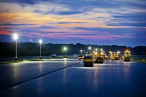 Paving an airport runway at sunset with multiple Sakai asphalt rollers.