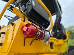 Optional factory installed 5lb ABC fire extinguisher and mount kit for the R2H-4 three wheel asphalt compactor mounted behind one of the operator seats. Shown at an angle.