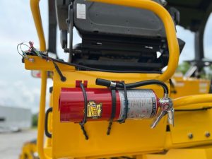 Optional factory installed 5lb ABC fire extinguisher and mount kit for the R2H-4 three wheel asphalt compactor mounted behind one of the operator seats. Shown straight behind.