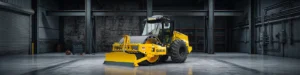 A new SAKAI SV544-1 84 inch soil compactor with strike off blade, cab, and smooth shell kit is dimly lit inside an industrial facility.
