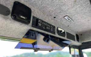 Forward view inside the SV544 or SV414 soil compactor enclosed cab showing the radio head unit, audio speakers, wiper control switches, and sun visor.