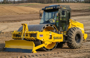 A new SAKAI SV544-1 series 84 inch soil compactor with leveling blade and smooth shell kit compacts soil on a typical site prep job.