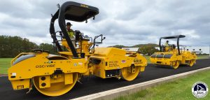 Two SAKAI SW884ND asphalt rollers equipped with the new Guardman Echelon Mode roll in tandem formation in front of the SAKAI factory. A Heavy Equipment Guide 2025 Top Introductions logo is in the bottom right of the image.