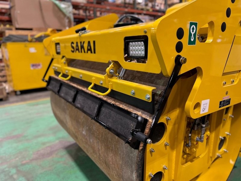 Front side view of coco mat assembly mounted on a SAKAI SW774 66 inch 11 ton asphalt roller with mat in down position and scraper in down position.