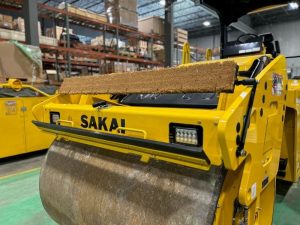 Coco mat assembly mounted on a SAKAI SW774 66 inch 11 ton asphalt roller with bracket in up position and scraper in up position.