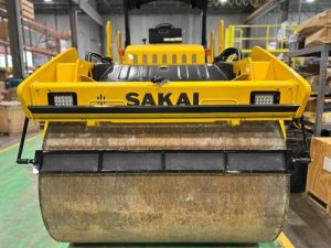 Front drum view of coco mat assembly mounted on a SAKAI SW774 66 inch 11 ton asphalt roller with mat in down position and scraper in up position.