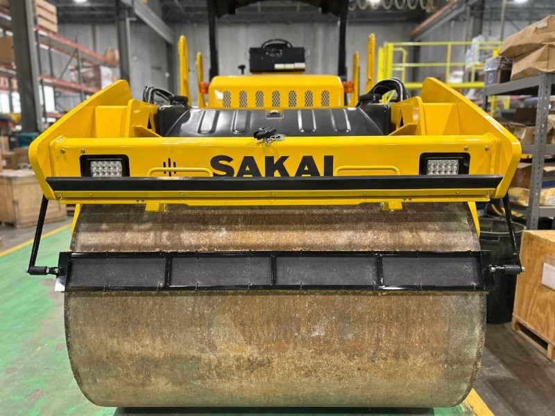 Front drum view of coco mat assembly mounted on a SAKAI SW774 66 inch 11 ton asphalt roller with mat in down position and scraper in up position.