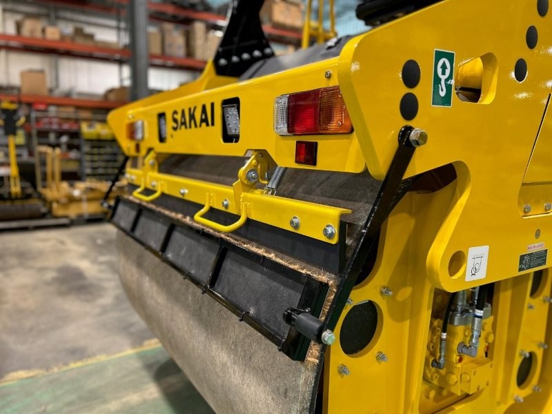 Rear drum side view of coco mat assembly mounted on a SAKAI SW774 66 inch 11 ton asphalt roller with mat in down position and scraper in down position.