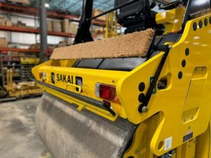 Rear side view of coco mat assembly mounted on a SAKAI SW774 66 inch 11 ton asphalt roller with mat in up position and scraper in up position.