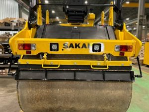 Rear drum view of coco mat assembly mounted on a SAKAI SW774 66 inch 11 ton asphalt roller with mat in down position and scraper in down position.