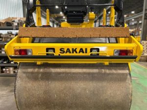 Rear view of Coco mat assembly mounted on a SAKAI SW774 66 inch 11 ton asphalt roller with mat in up position and scraper in up position.