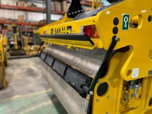 Rear side view of coco mat assembly mounted on a SAKAI SW774 66 inch 11 ton asphalt roller with mat in down position and scraper in up position.