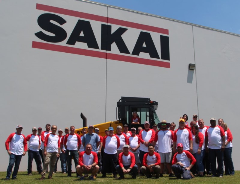 Sakai America employees pose in front of a SV544 cab soil compactor outside the USA factory for the 20th anniversary celebration of US manufacturing.