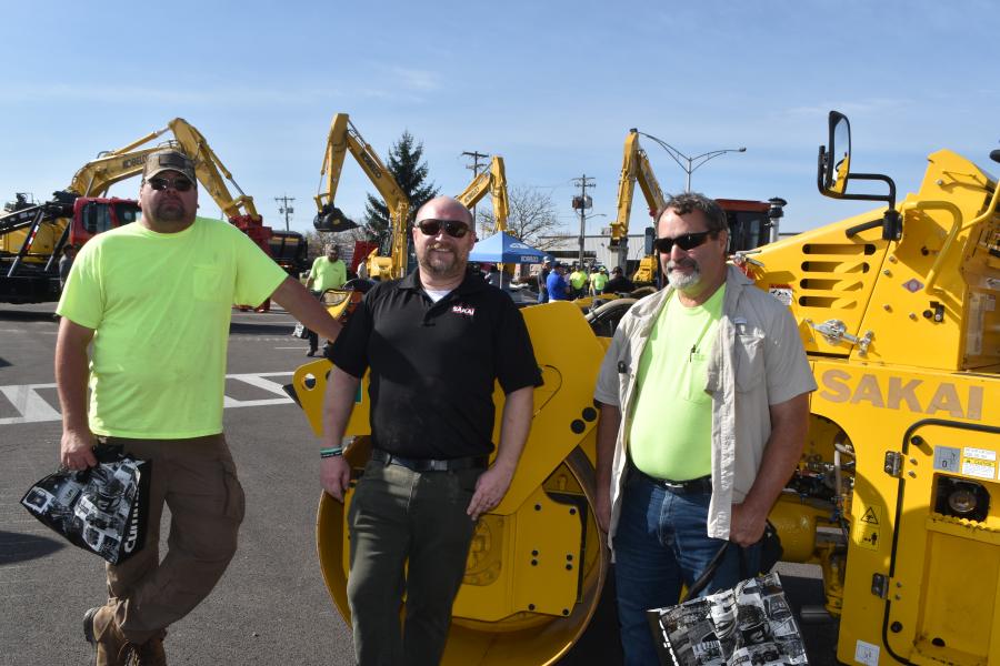 SAKAI America manager of Sales Brad Belvin poses for a photo with paving contractors and an SW654ND oscillating asphalt roller at dealer Tracey Road Equipment's annual open house event in Syracuse.