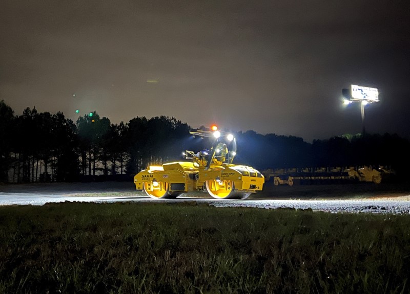 Fully illuminated SAKAI SW884 79" 14 ton double drum asphalt roller at night showing the optional LED upgrade, LED work light kit, and LED drum light or mat light kit.