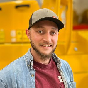 A Sakai America US factory employee smiles in front of a yellow asphalt roller.