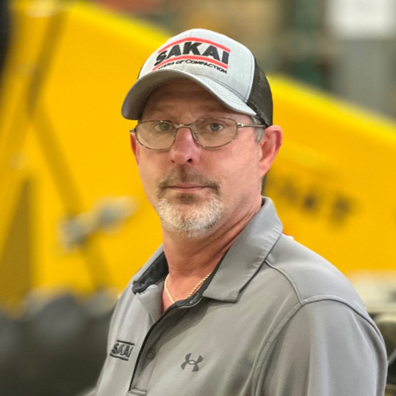 Sakai service support employee in front of an SV544 soil compactor at the final inspection station of our USA assembly line.