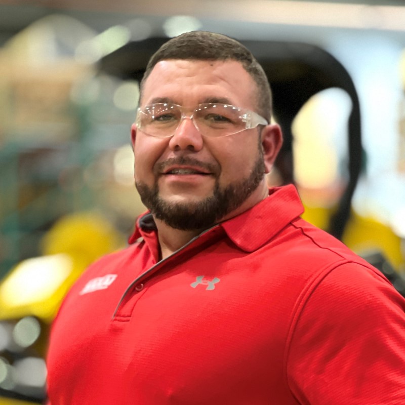 Sakai quality control testing employee profile photo in front of a soil compactor on our production line in Adairsville, GA.